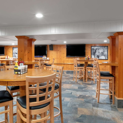 The image shows a restaurant or bar with wooden columns and tables, high chairs, multiple TVs on the walls, and framed photos.