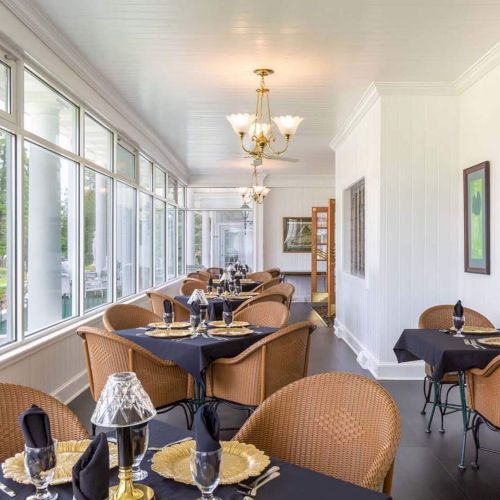 A bright dining area with wicker chairs, black table settings, large windows, and decorative lighting.