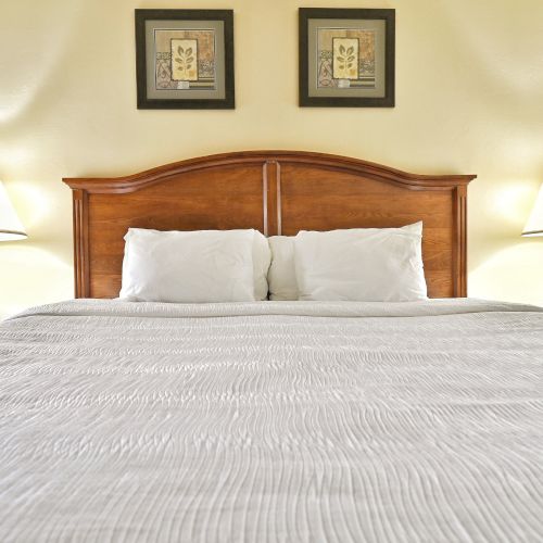 A neatly made bed with white linens, flanked by two lamps and artwork above the headboard completes the room.