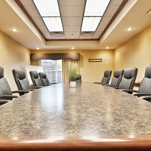 A conference room with a long table, several chairs, a plant in the center, and framed artwork on beige walls, under bright lights.