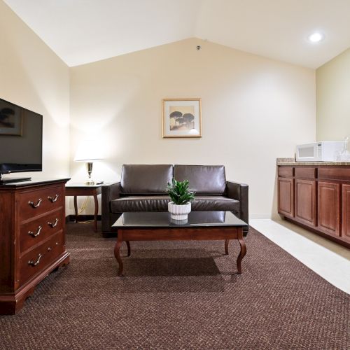 A cozy room with a TV, brown sofa, coffee table, cabinets, and a framed picture on the wall, all on a carpeted floor.