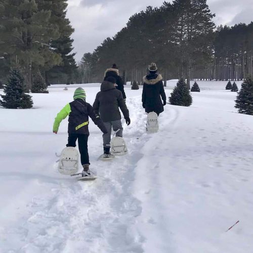 A group of people, including a child, is snowshoeing along a snowy path surrounded by trees.