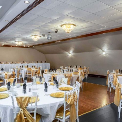 An elegant banquet hall with white tablecloths, gold decor, and neatly arranged chairs set for an event.
