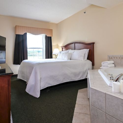 A hotel room features a bed, TV, window, and an in-room jacuzzi with candles and a plant.