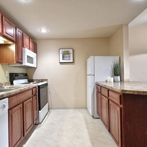 A kitchen with wooden cabinets, stove, microwave, refrigerator, dishwasher, and countertop with decor and dining area.