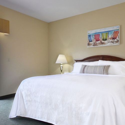 A cozy bedroom featuring a large bed, two lamps, and a side table, with a balcony view through a sliding door.