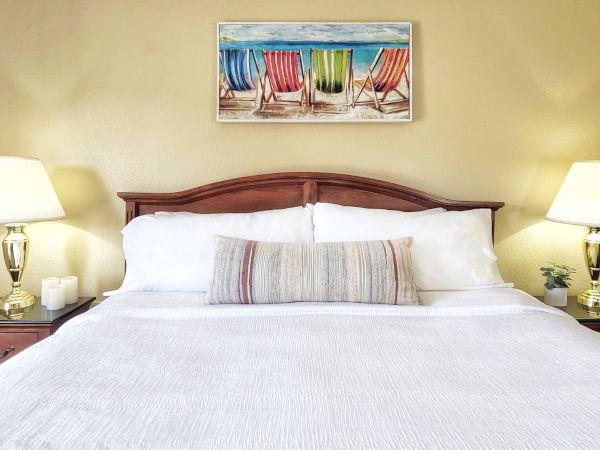 A bedroom with a neatly made bed, two side tables with lamps, and a beach-themed painting above the headboard ends the sentence.