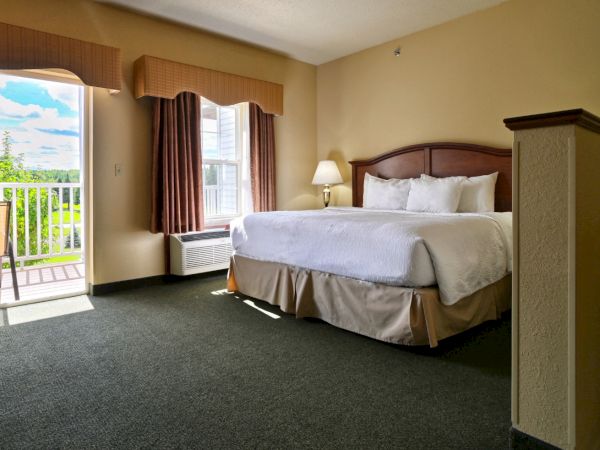 A spacious hotel room with a large bed, bedside lamp, and curtains over a sliding glass door leading to a balcony.