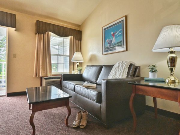 A cozy living room with a leather couch, coffee table, side tables with lamps, a picture on the wall, and shoes on the floor.