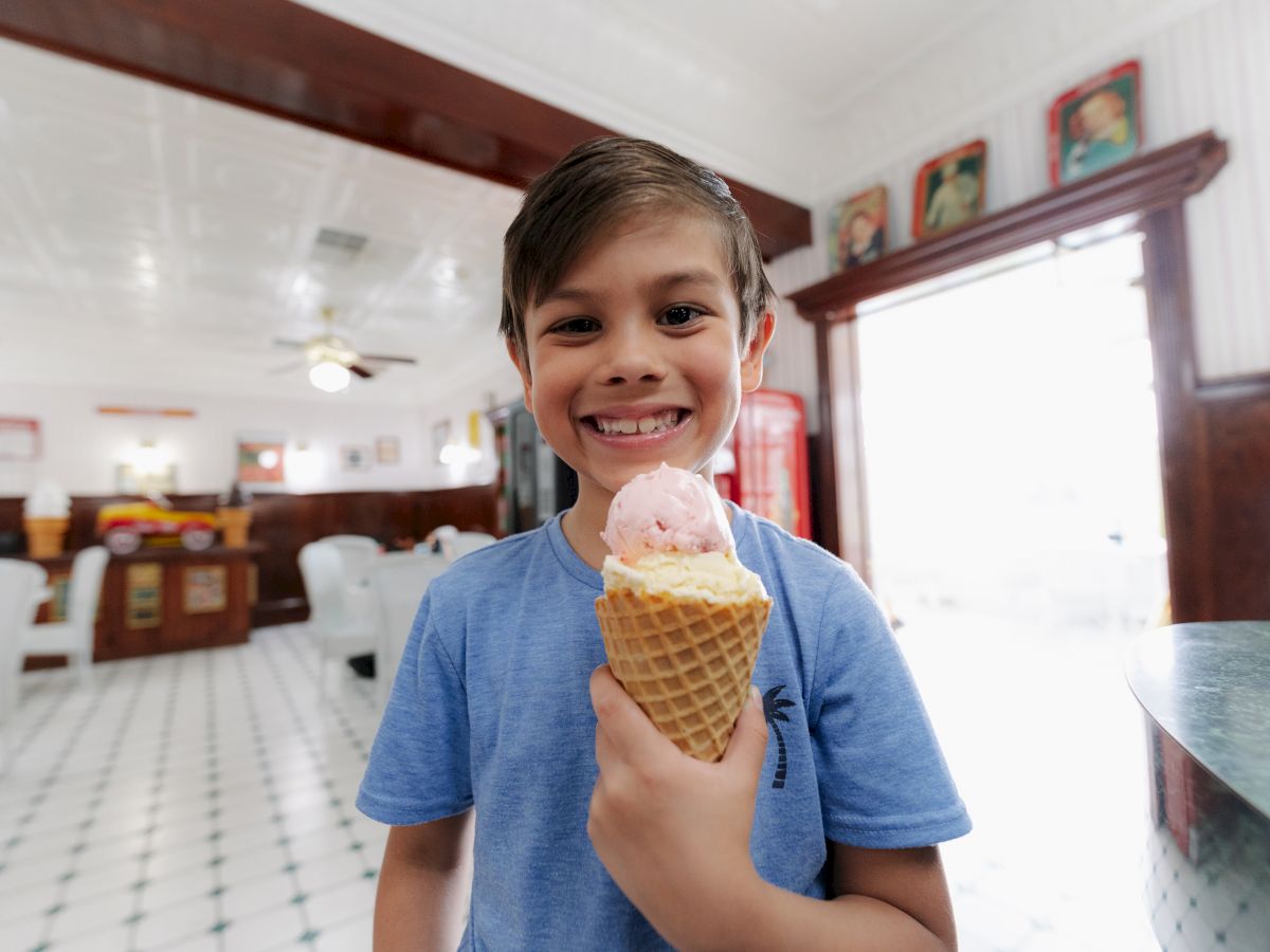 A child smiling and holding an ice cream cone inside a brightly lit room with a vintage interior design.