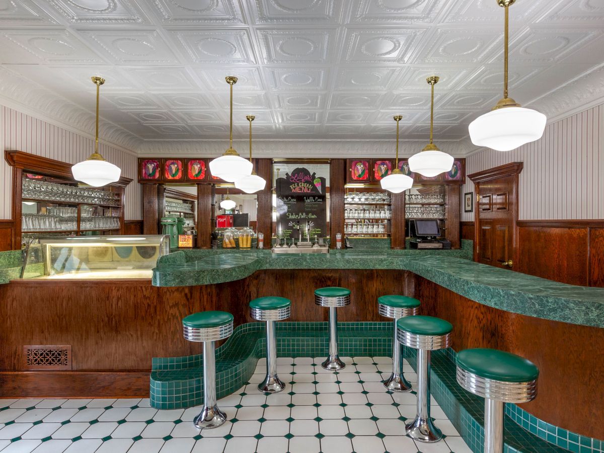 This image shows a vintage-style diner with green stools, white pendant lights, and a tiled floor, evoking classic American design.