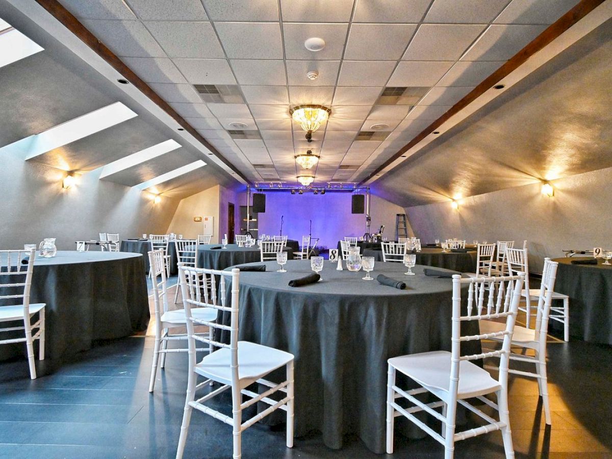 The image shows a decorated event hall with round tables covered in gray tablecloths and white chairs under soft lighting.