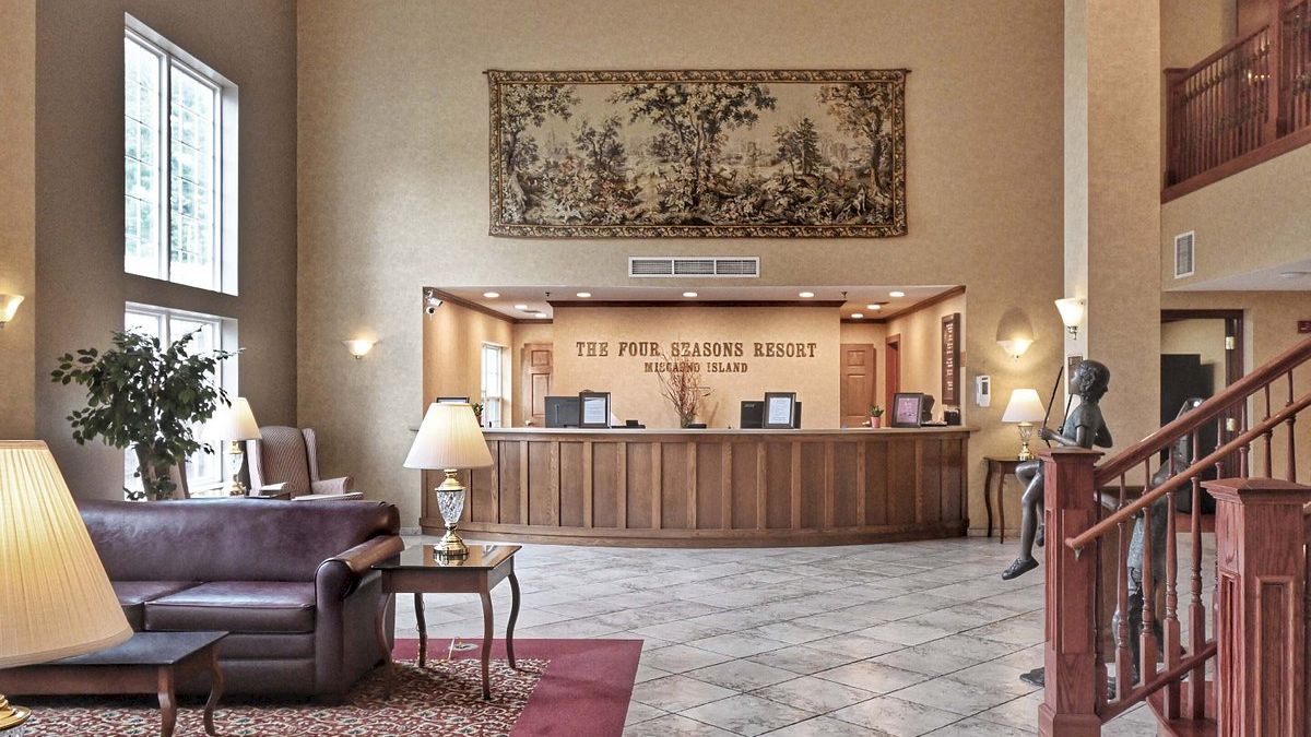 The image shows a hotel lobby with tiled floors, a reception desk, a seating area with a couch, lamps, and a staircase. Ending the sentence.