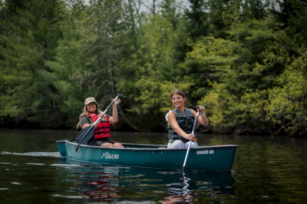 Two people are canoeing on a calm lake surrounded by lush greenery.