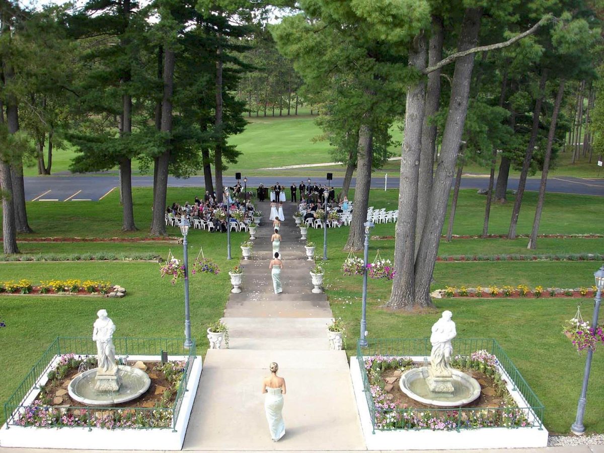 An outdoor wedding ceremony on a landscaped garden walkway, with guests seated on both sides and the bride walking down the aisle.