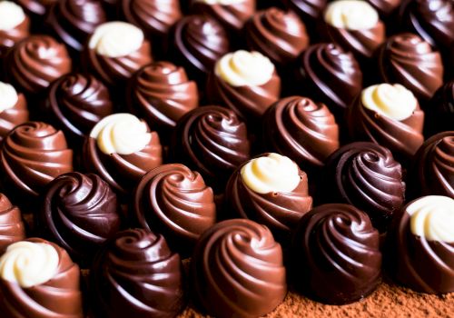 The image shows a close-up view of rows of swirled chocolate candies with white and dark chocolate decorations on top, arranged neatly on a surface.
