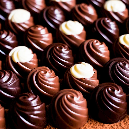 The image shows a close-up view of rows of swirled chocolate candies with white and dark chocolate decorations on top, arranged neatly on a surface.