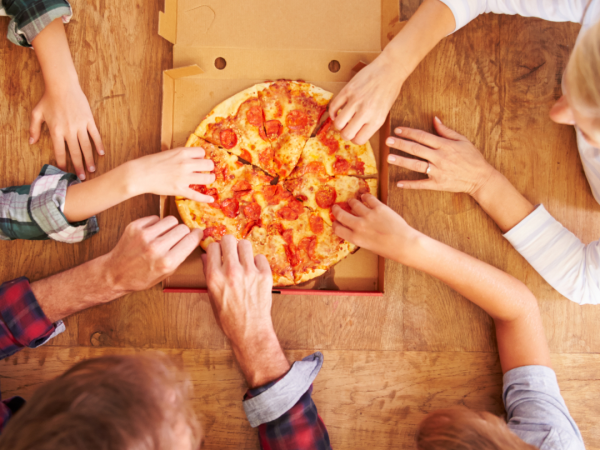 A group of people are reaching for slices of pepperoni pizza on a wooden table.
