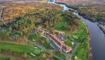 Aerial view of a large building complex surrounded by golf courses, trees, and a river, with autumn foliage in the landscape.